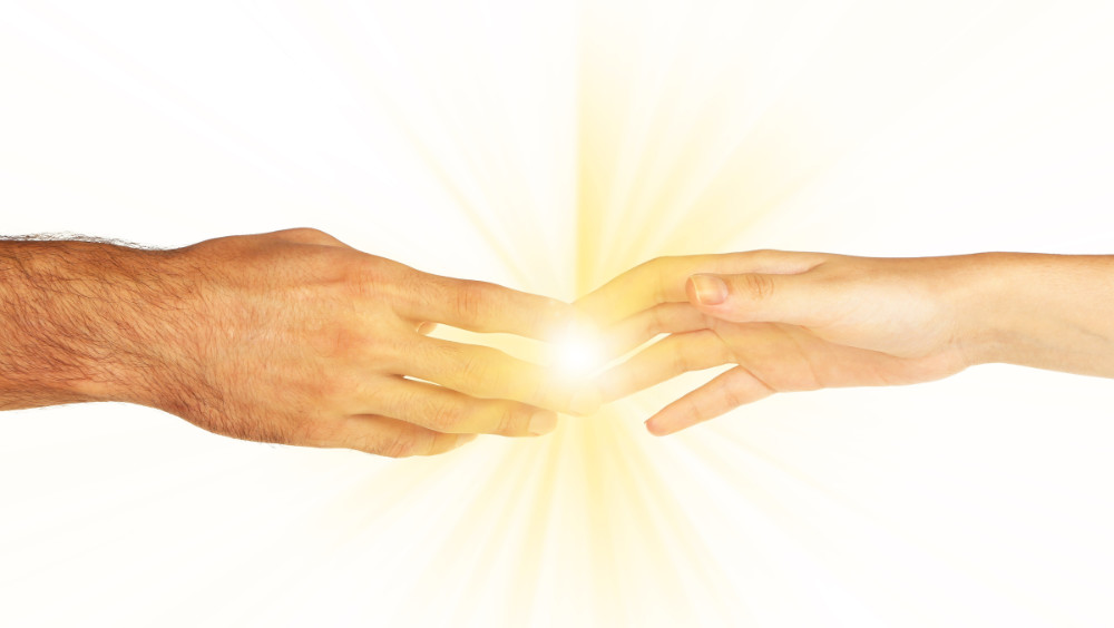 Das Bild zeigt zwei Hände, wobei ein Lichtstrahl das Geben und Empfangen von Energie darstellt. Das Empfangen von Energie in Heilabsicht unterstützt jeden Menschen dabei, zurück zur Selbstliebe zu finden.