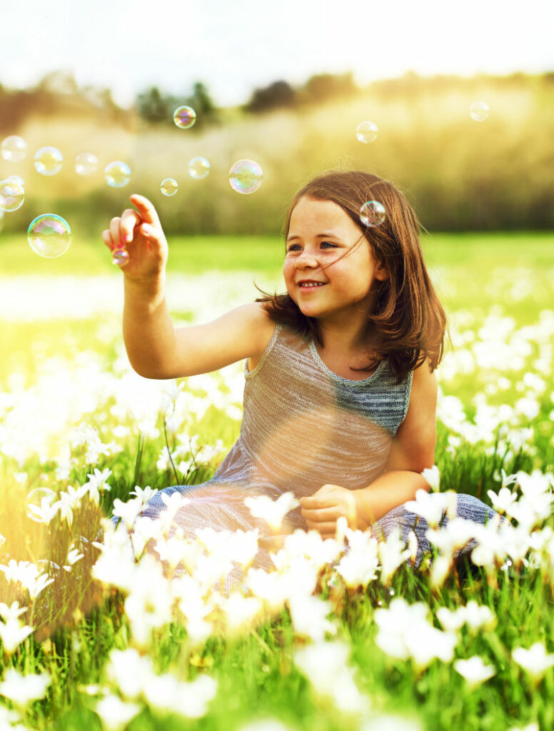 Das Foto zeigt ein spielendes Mädchen auf einer Blumenwiese, das lächelt. Damit steht es für jenes innere Glück, dass die Selbstliebe einschließt. 