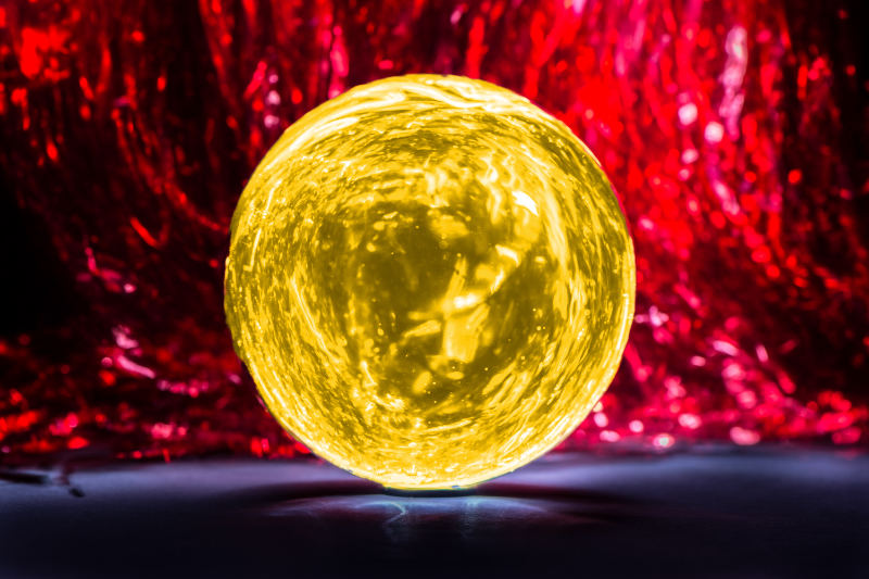 Das Foto zeigt eine gelbe Glaskugel vor rotem Hintergrund. Das Rot symbolisiert etwa die Wut eines anderen. Eine Technik zum Schutz ist es, sich vorzustellen, man befände sich innerhalb einer hermetisch geschlossenen Glaskugel.