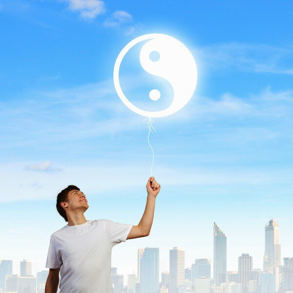 Das Foto zeigt einen Mann, der einen Luftballon mit dem Yin-und Yang-Zeichen in der Hand hält. Im Hintergrund ist eine Skyline zu sehen. Das ist ein Synonym dafür, dass spirituelle Werte einen guten Ruf in der Gesellschaft genießen. 